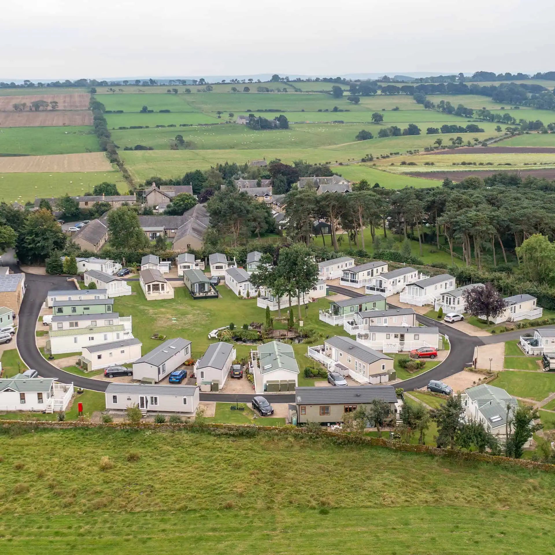 Aerial view of a holiday park with caravans, surrounded by rural countryside with rolling hills, farmland, and a small village - Club4.