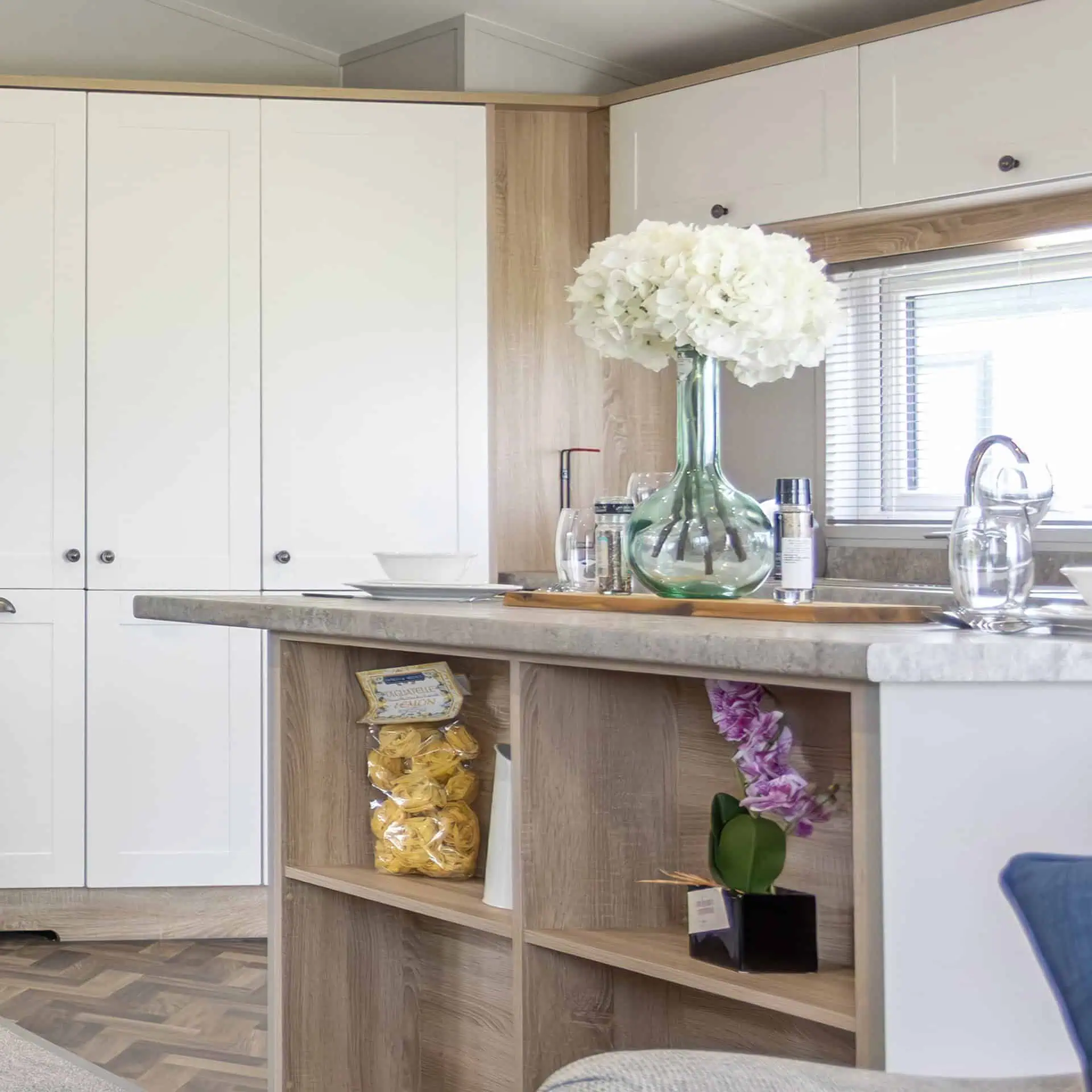 Modern kitchen interior with white cabinets and wooden accents and a decorative glass vase with white hydrangeas - Club4.