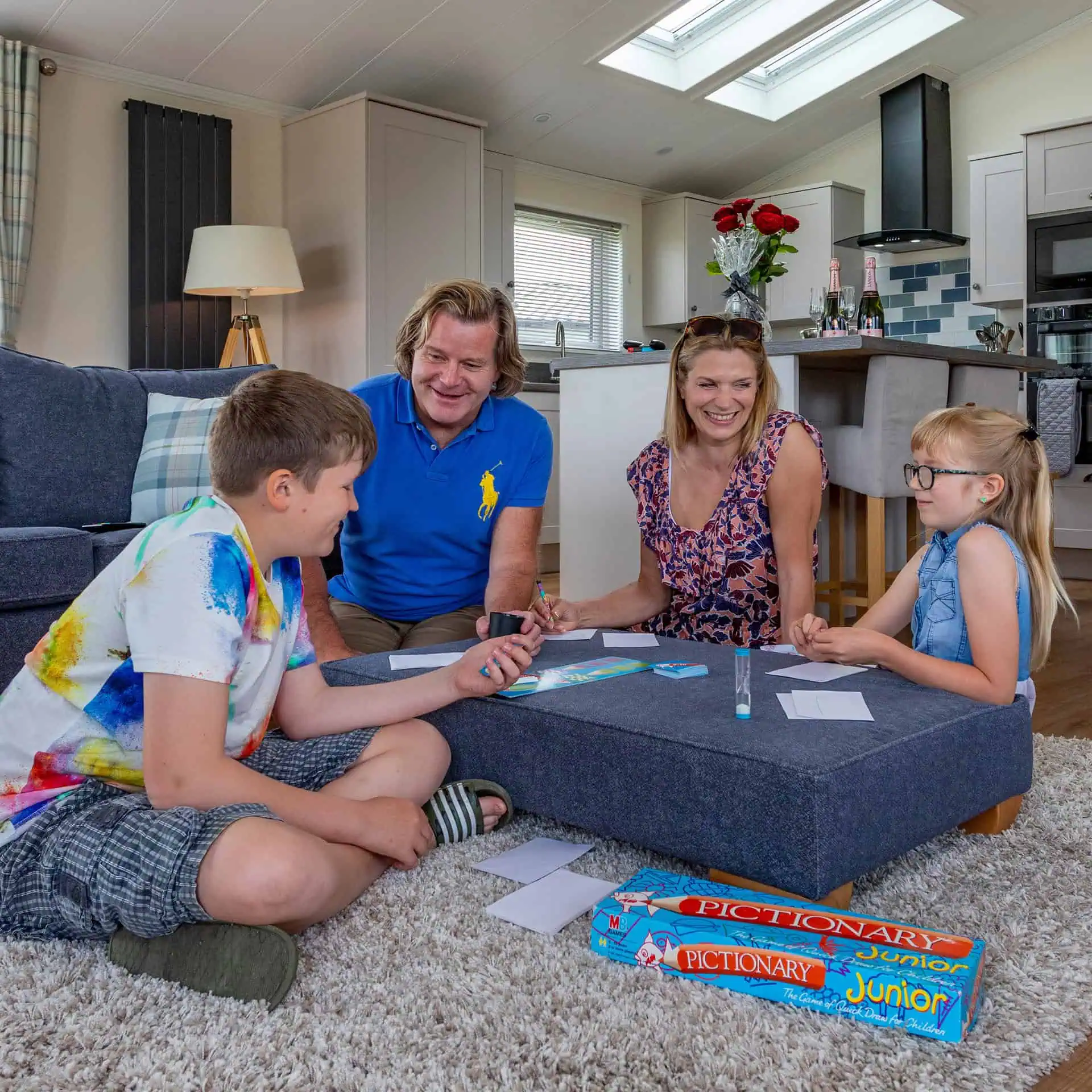 Family playing Pictionary Junior together in a holiday home living room - two adults and two children gathered around a coffee table - Club4.