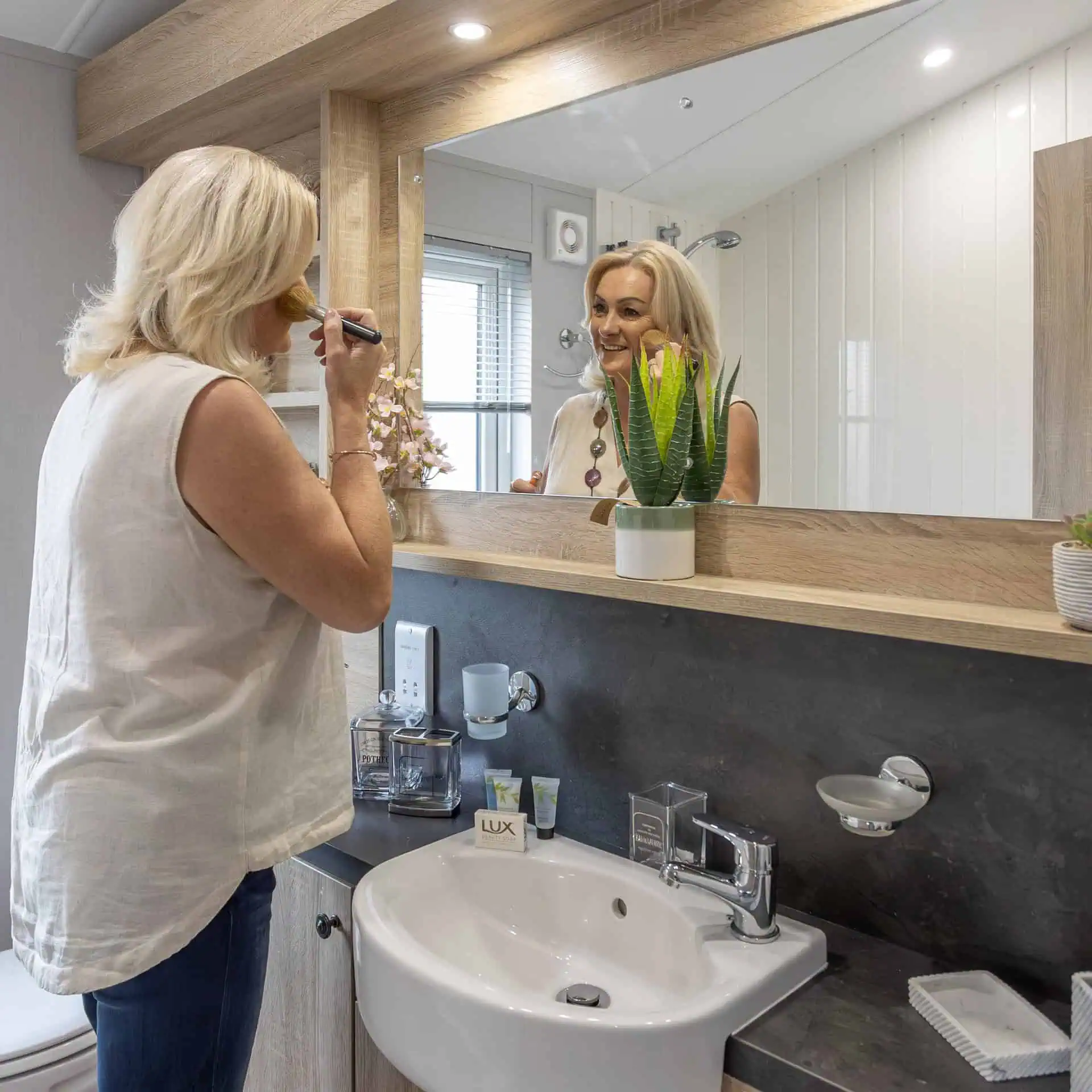 A woman applying makeup in a modern bathroom mirror - Club4.