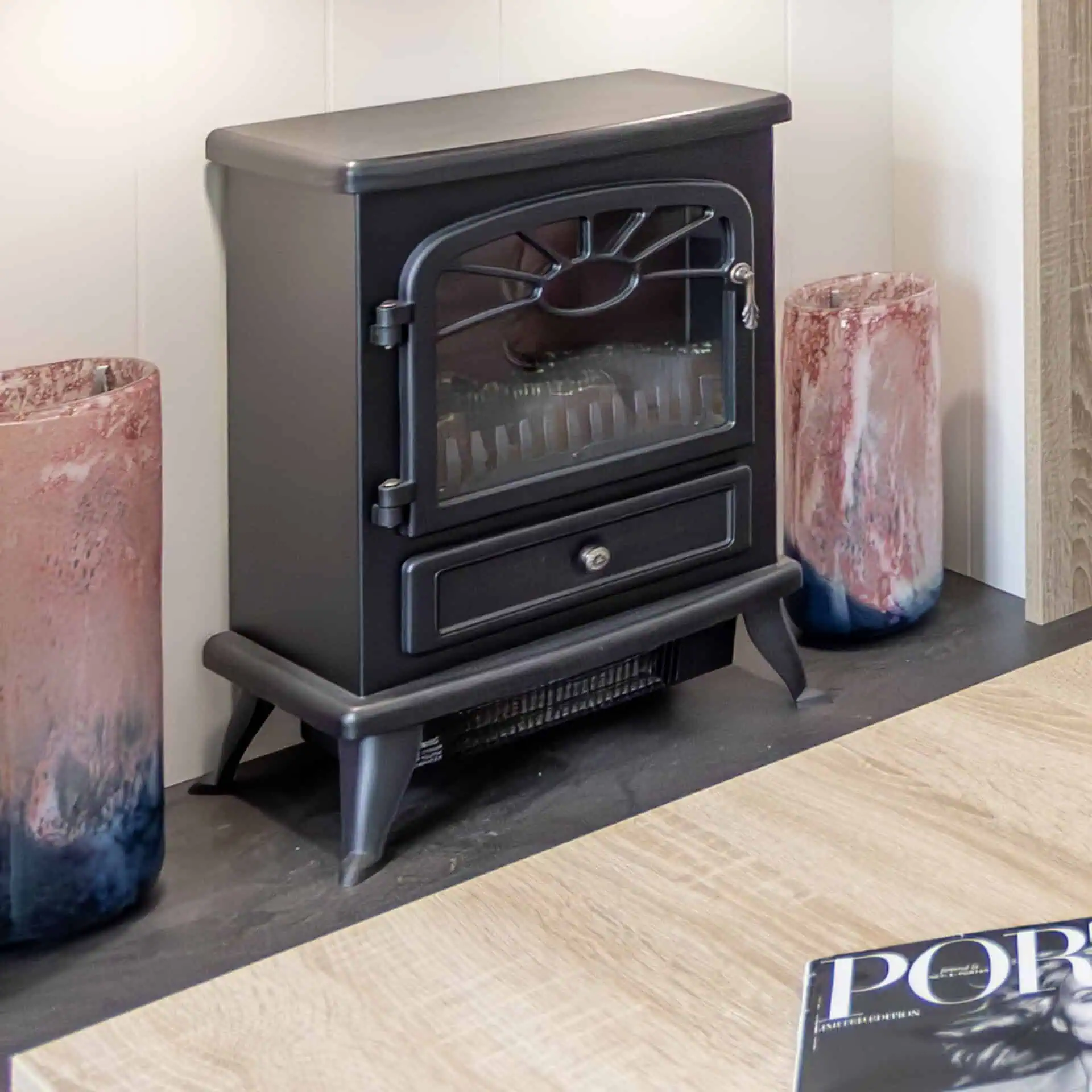 A black electric fireplace heater, flanked by pink and blue decorative glass vases against a white wall - Club4.