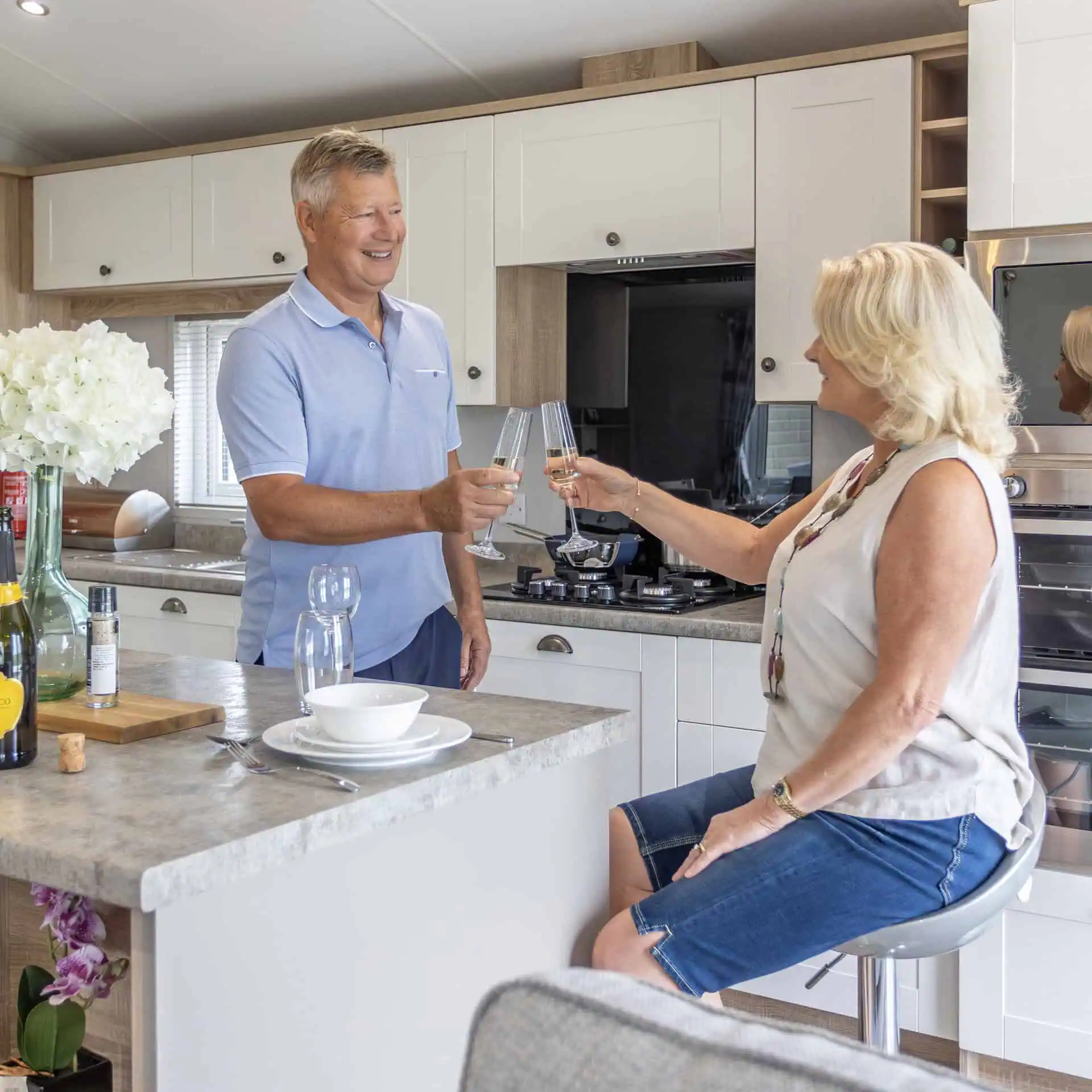 Two people toasting with champagne glasses in a modern kitchen with white cabinets - Club4.