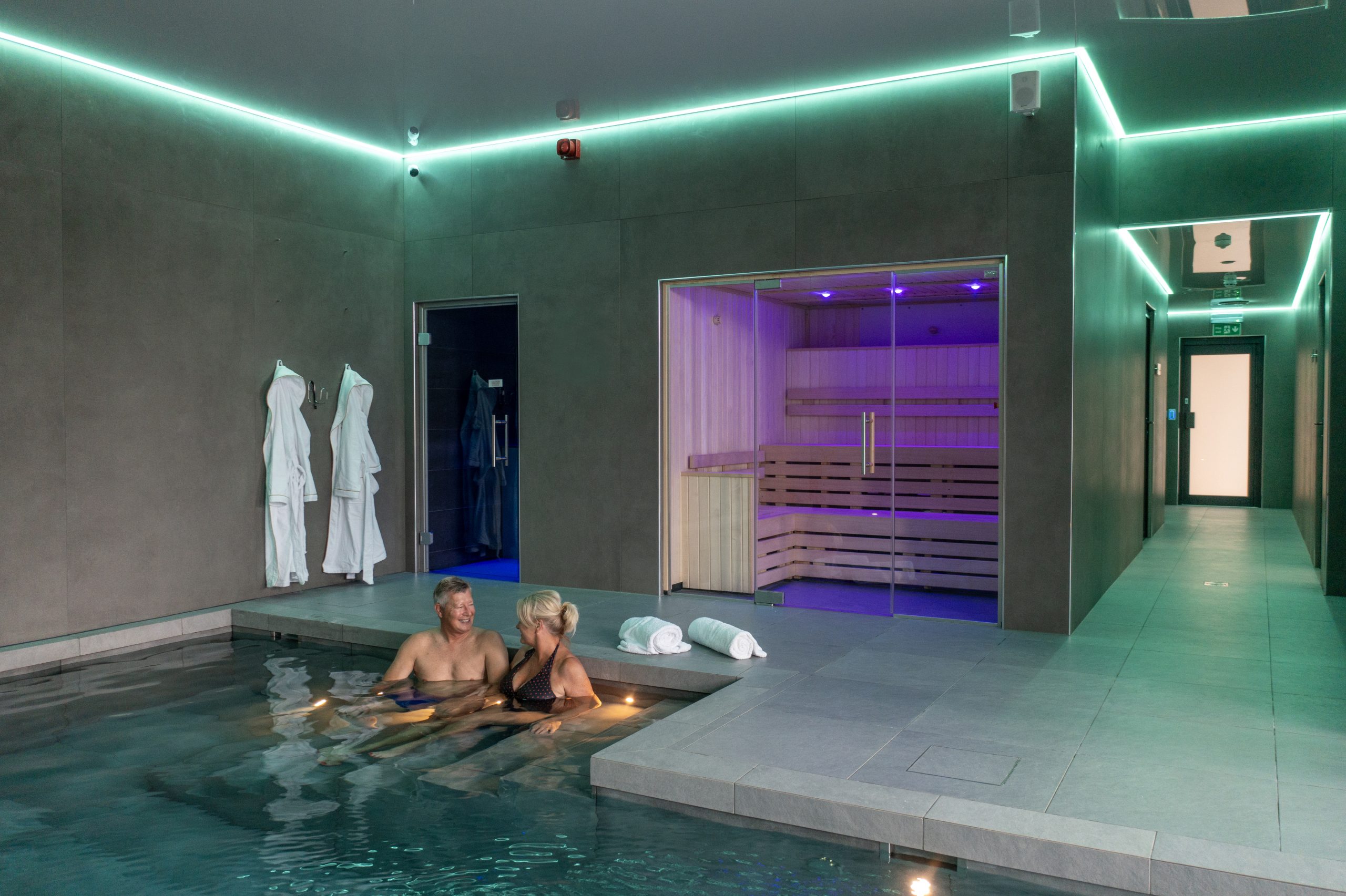 A couple in an indoor pool, smiling. Modern lighting inside and a sauna behind them. Investment Opportunity at Heathergate Boutique Holiday Park: Willerby Portland Lodge