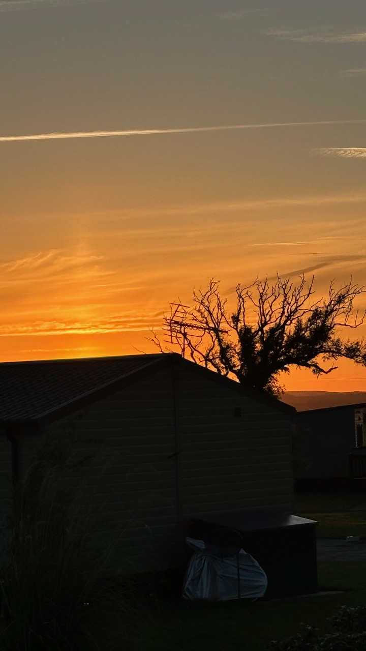 Orange sunset over a tree line and caravans.