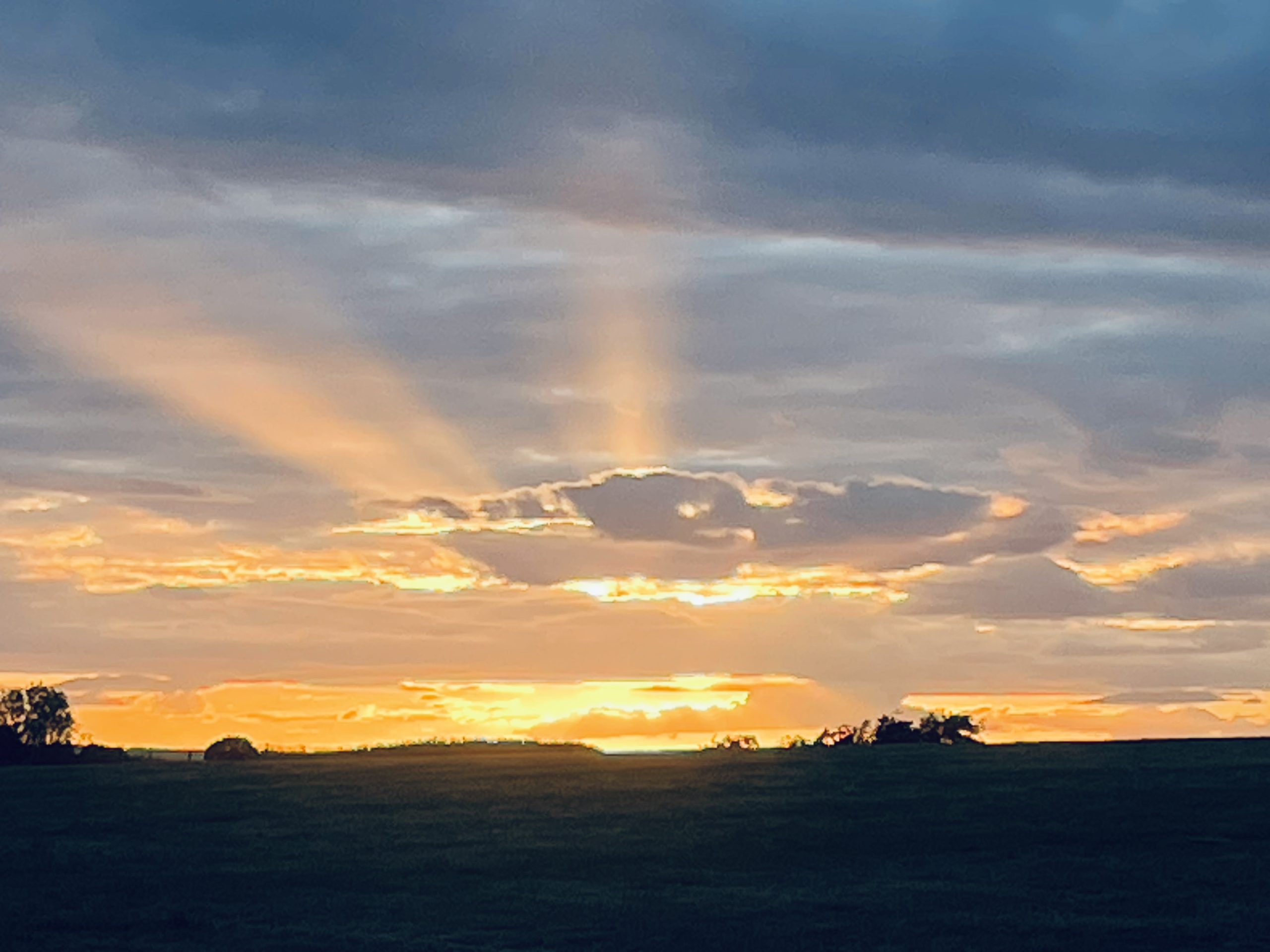 Glowing sunset with light beams breaking through clouds over a grassy horizon.