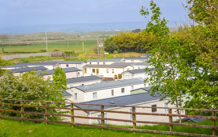 A scenic view of a mobile home park with rows of caravans and a backdrop of countryside hills.