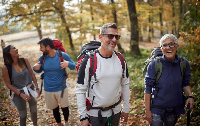 Group of smiling hikers walking through an autumn forest.